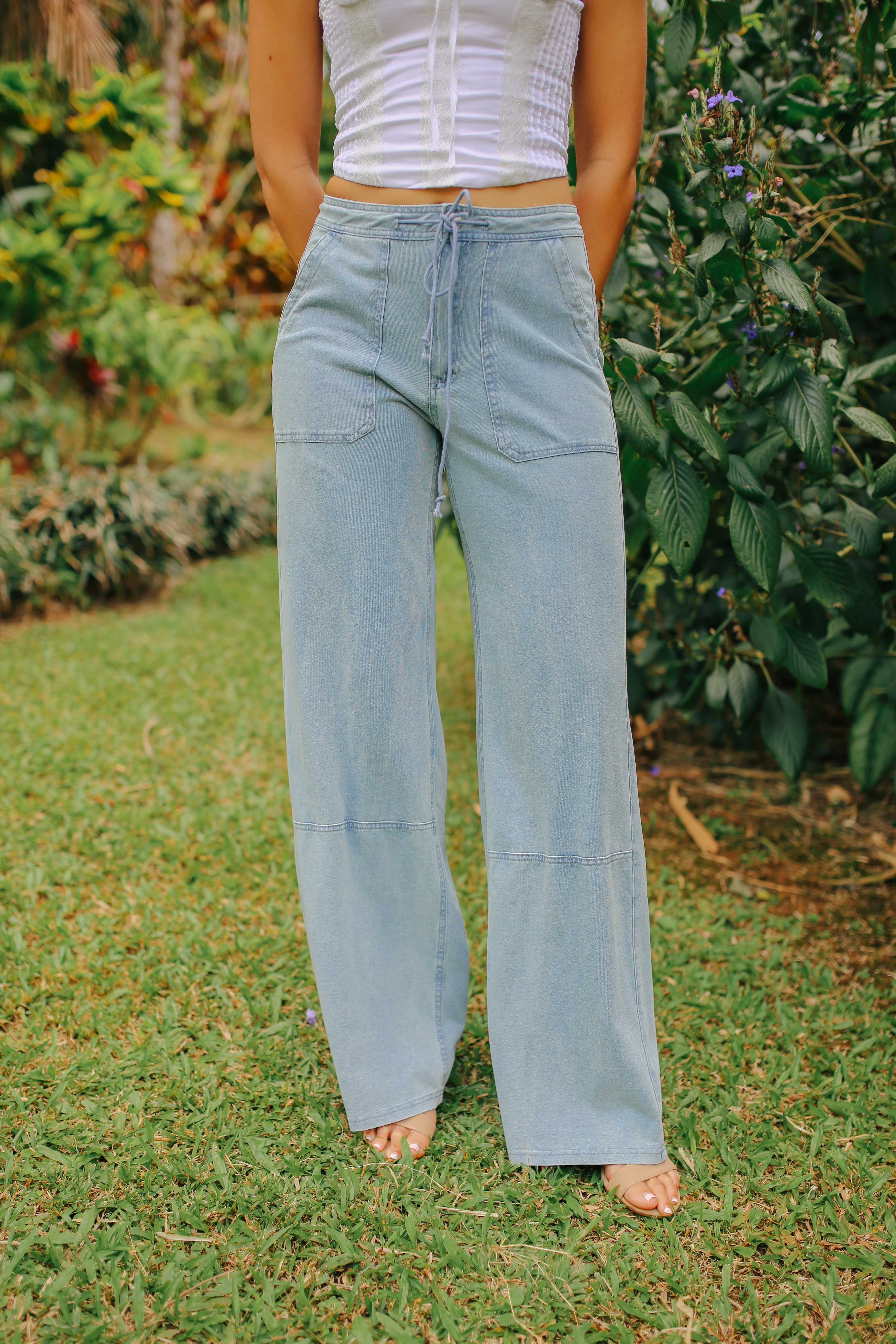 A woman standing outdoors wearing blue wide-leg cargo pants and a white off-shoulder top.