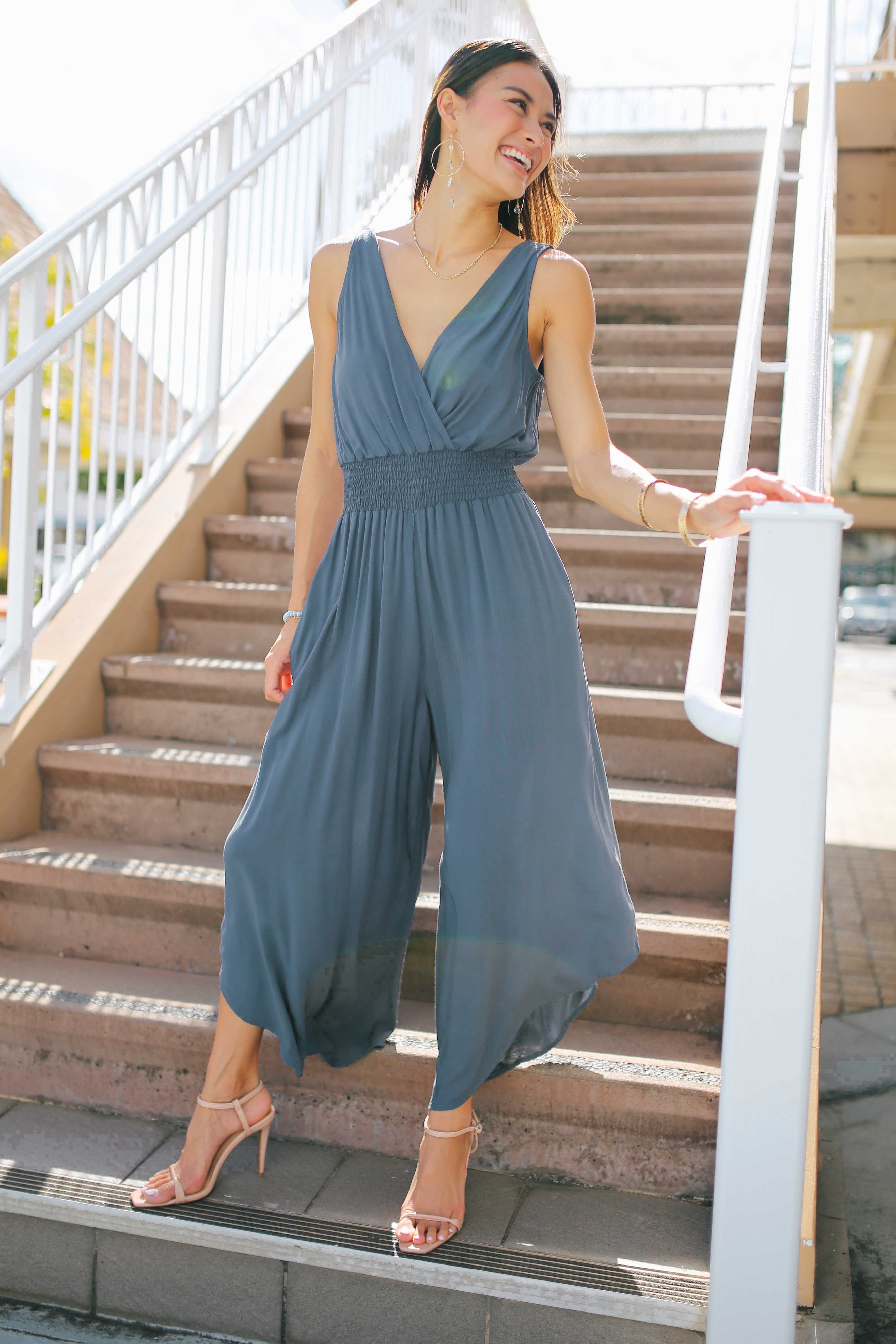 Woman in a blue jumpsuit standing on outdoor steps.